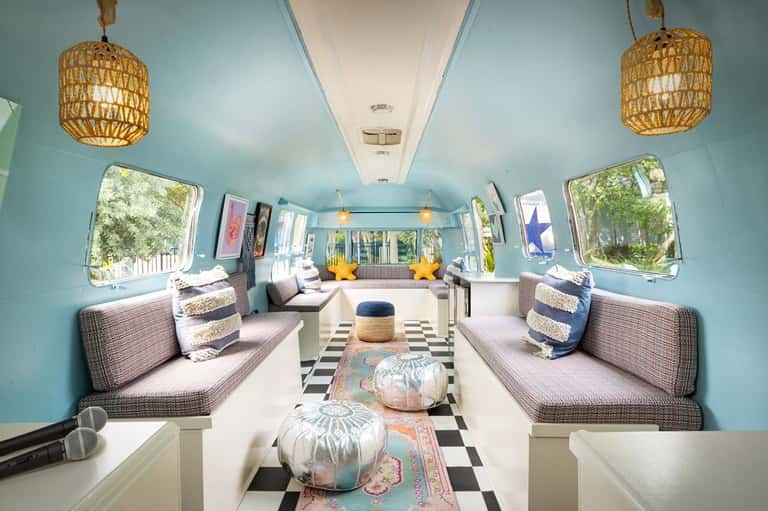 Turquoise vintage airstream trailer interior with dual seating, woven pendant lights, and windows