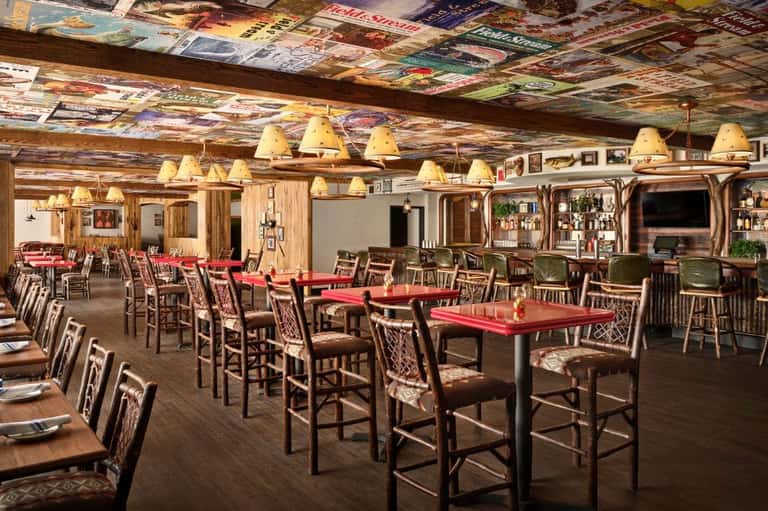 Rustic lodge dining room with red tables, wooden chairs, exposed beams, and vintage decor throughout.