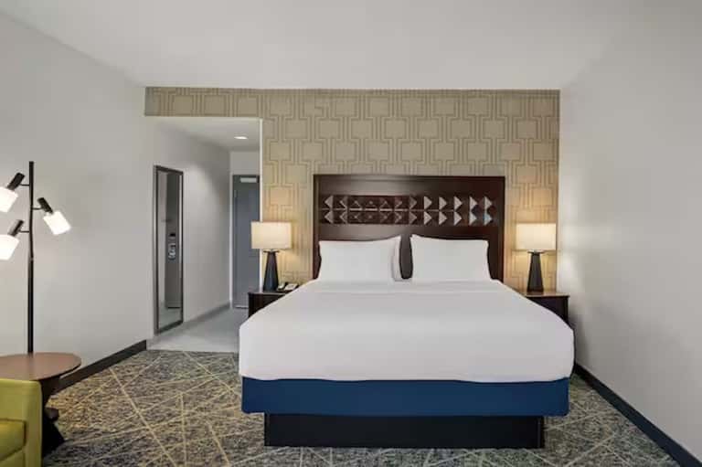Hotel bedroom with queen bed, geometric headboard, patterned wallpaper, and modern furnishings