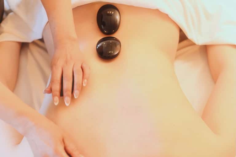 Therapist placing two heated black massage stones on client's back during spa treatment