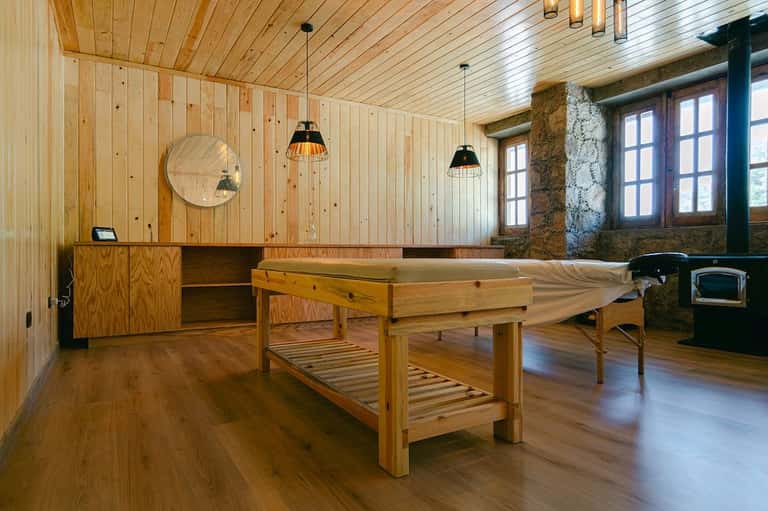 Wooden spa room with massage table, wooden bathtub, fireplace, and rustic stone elements