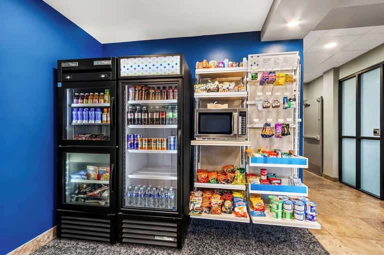Hotel convenience store with refrigerated beverage cases, wall-mounted snack displays, and blue accent wall