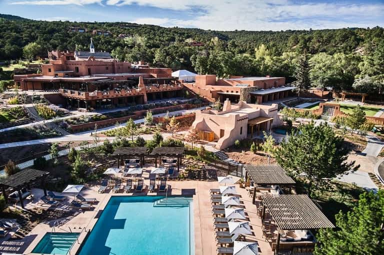 Aerial view of a terracotta-colored resort with pools, loungers, and surrounding forested landscape