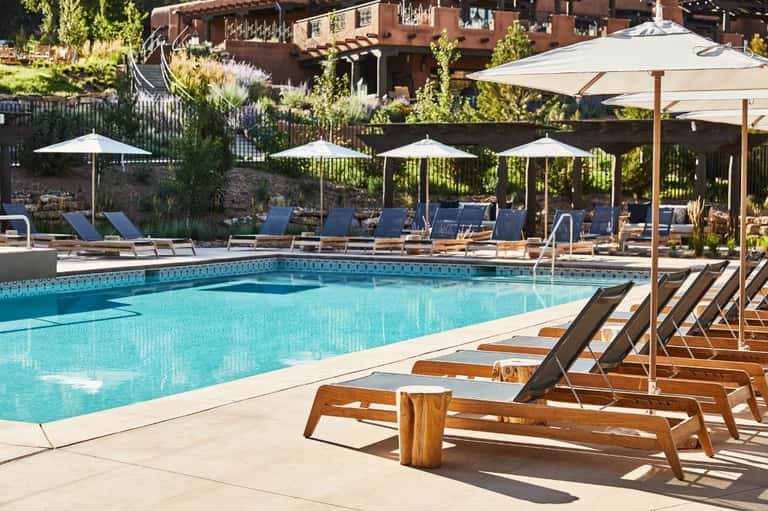 Lap pool with rows of wooden loungers, white umbrellas, and rocky hillside landscape