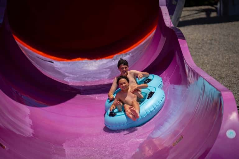 Two children on a blue inflatable tube sliding down a vibrant purple water slide