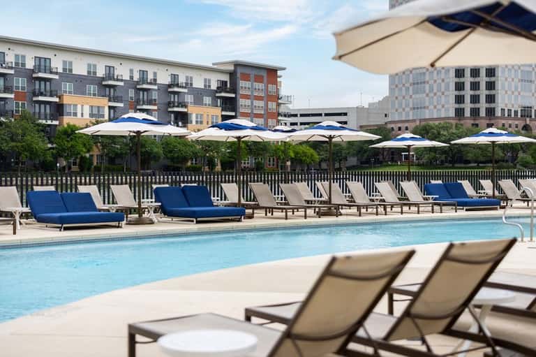 Resort pool with blue loungers, white umbrellas, and residential buildings nearby