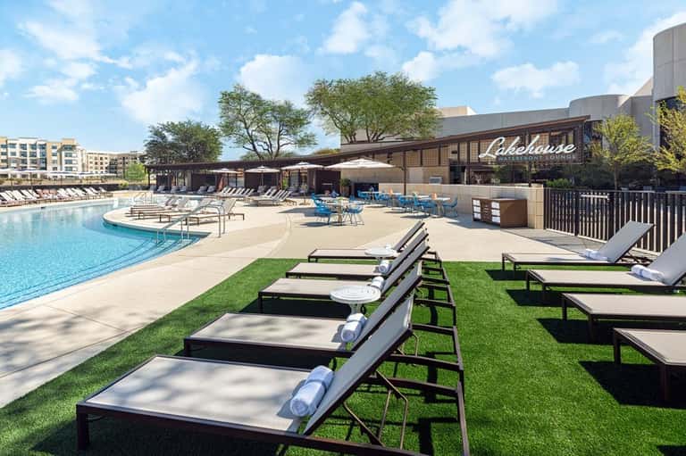 Lakehouse resort pool area with loungers, umbrellas, grass, and modern architecture