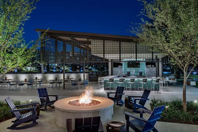 Nighttime outdoor lounge with fire pit, blue chairs, pergola, and bar area under starlit sky
