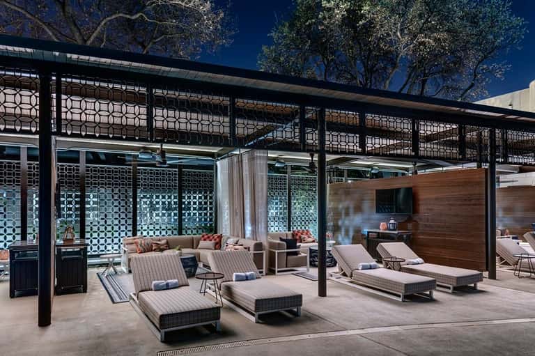 Covered poolside lounge with geometric patterned screens, striped loungers, and fireplace