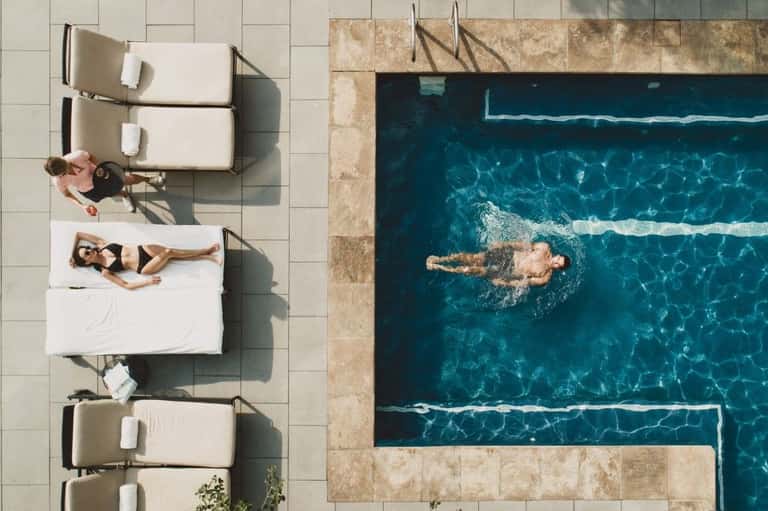 Aerial view of swimming pool with lane dividers, guests on loungers, and surrounding deck