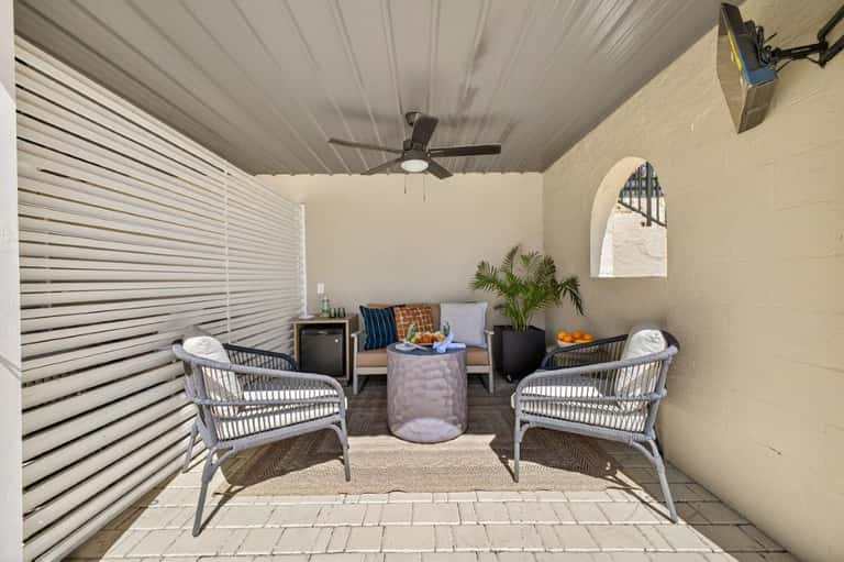 Covered patio lounge area with wicker chairs, potted plants, and modern furniture facing a stucco wall