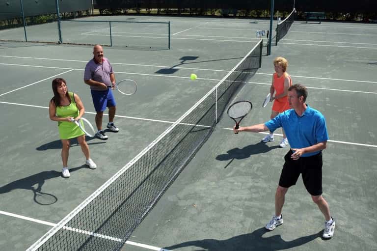 Four people playing doubles tennis on outdoor court in bright sunshine