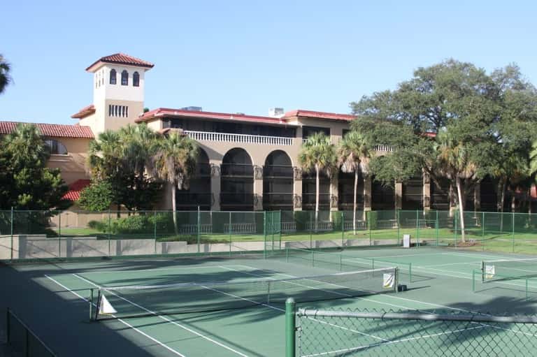 Spanish colonial-style building with arched windows and red tile roof overlooking tennis courts