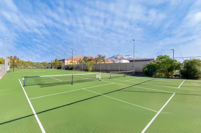 Multiple professional tennis courts with white line markings and net posts under blue sky