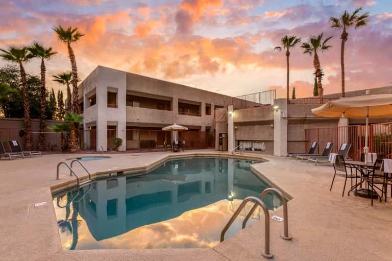 Resort pool at sunset with palm trees, lounge chairs, and modern concrete building