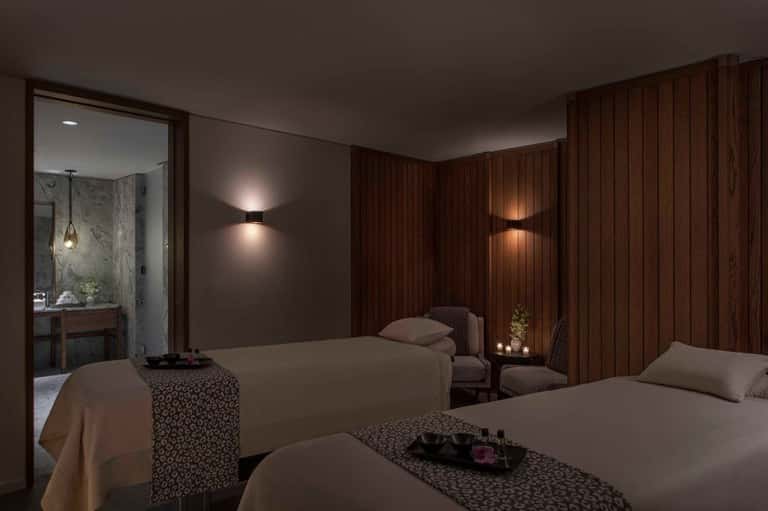 Luxury spa bedroom with dual beds, wood paneling, soft lighting, and ensuite bathroom