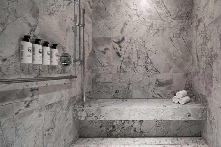 Marble spa shower with premium toiletries and rolled white towels on bench