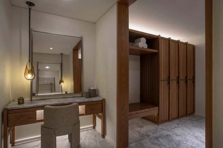 Luxury spa bathroom with wooden vanity, large mirror with pendant lights, and wooden closet cabinetry