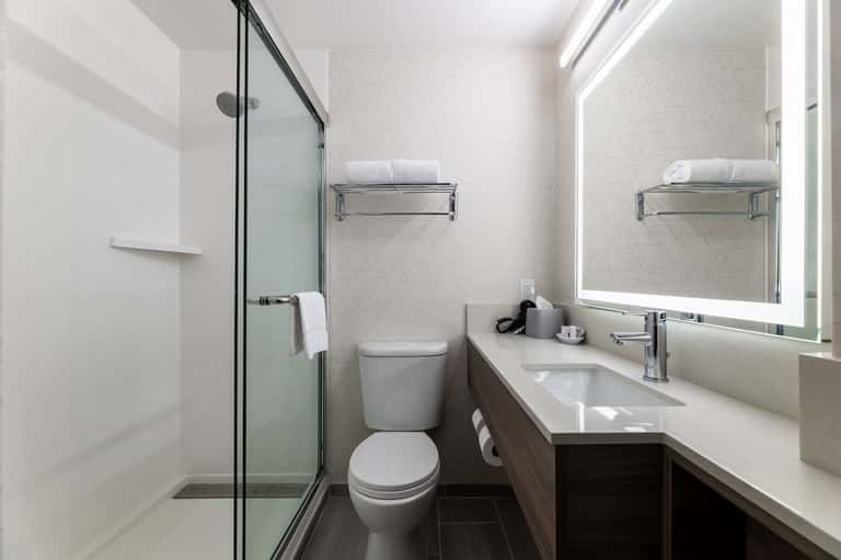 Clean bathroom with walk-in shower, white subway tile, illuminated mirror, and dark wood vanity
