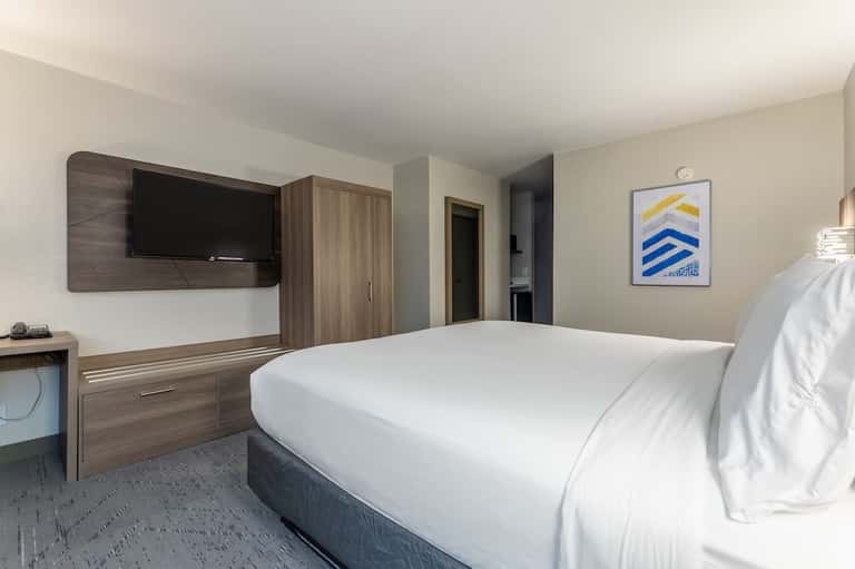 Contemporary hotel room featuring queen bed, wall-mounted TV, wood furnishings, and framed artwork