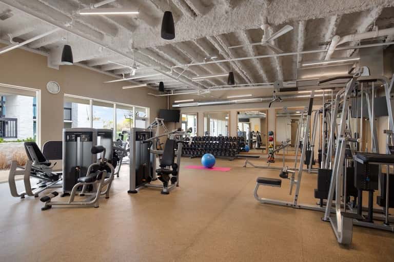 Spacious fitness center with cardio machines, weights, and windows overlooking grounds