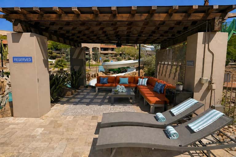 Shaded lounge seating with orange sectional, blue accents, and two gray loungers under wooden structure