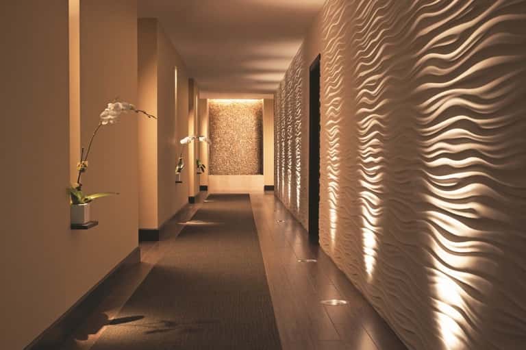 Elegant hallway with cream walls, textured wavy wall panels, accent lighting, and a white orchid