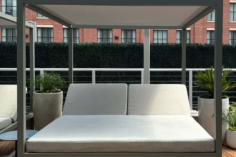 Modern gray pergola daybed with white cushions on rooftop terrace with city views