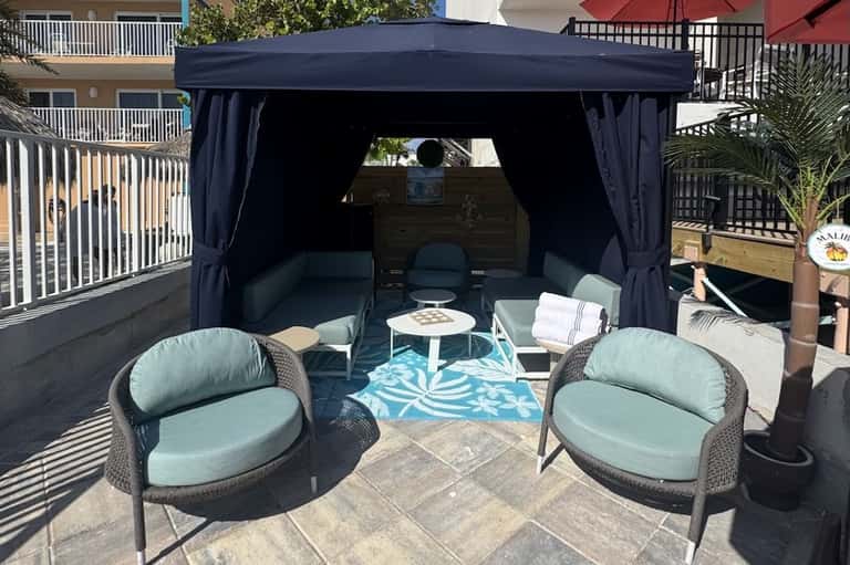 Outdoor cabana with dark navy curtains, mint green seating, and turquoise patterned rug
