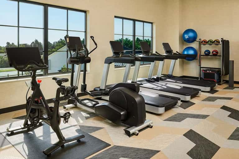 Modern fitness center with exercise bikes, treadmills, and strength training equipment by large windows