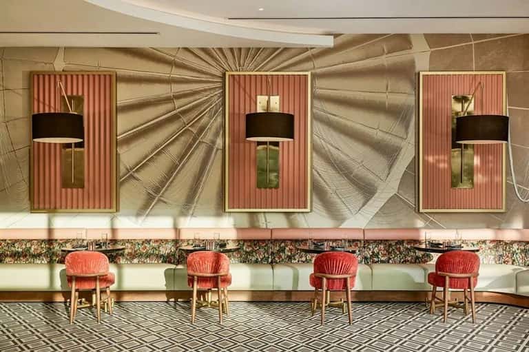 Elegant hotel bar with coral striped wall panels, black pendant lamps, geometric floor pattern, and red accent chairs