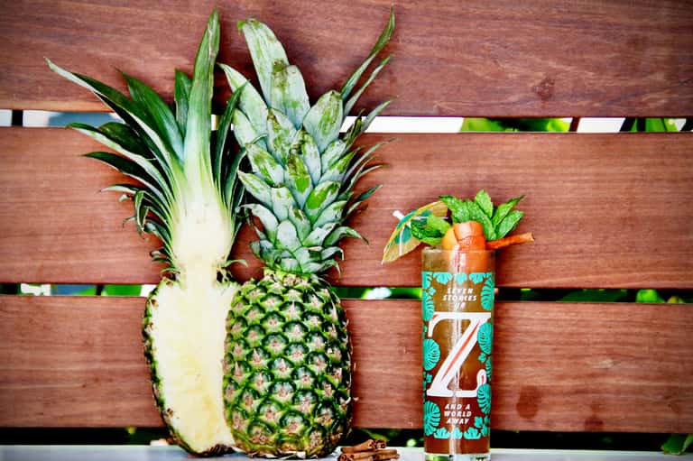 Sliced pineapple and tropical beverage on wooden deck railing with ocean view background