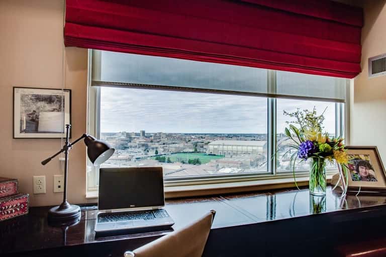 Hotel desk with laptop overlooking expansive city skyline through large window with burgundy roman shade