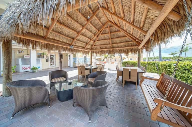 Covered tiki-roof patio with wicker seating, wooden swing, and ocean view at beachfront resort