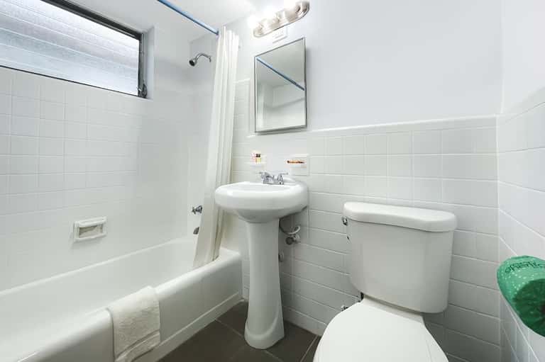 Clean white bathroom with pedestal sink, tile walls, mirror, and shower/tub combination