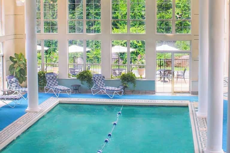 Indoor swimming pool with lane dividers, loungers, large windows, outdoor deck view with patio furniture