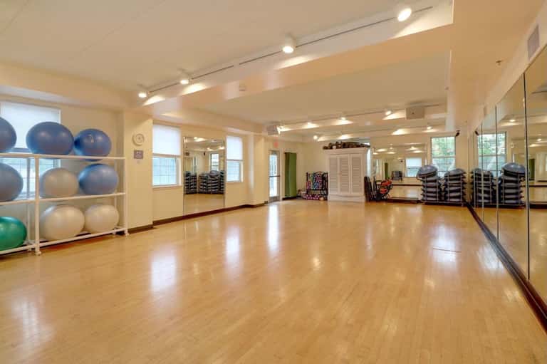 Fitness studio with wooden floors, exercise balls, mirror wall, windows, and fitness equipment storage