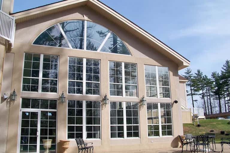 Large residential pool house with extensive windows, arched transom window, patio seating area