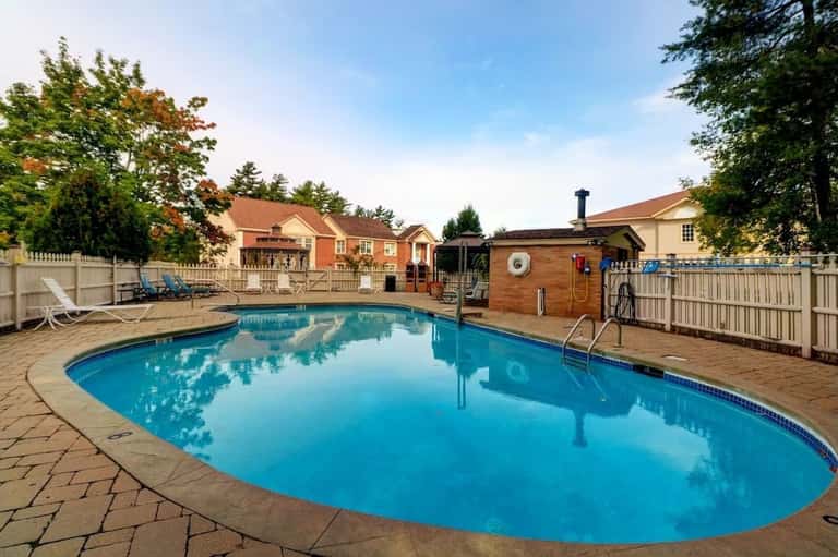 Outdoor resort swimming pool with brick patio, white fence, spa hot tub, lounge chairs, residential buildings
