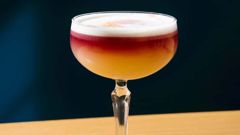 Layered craft cocktail with red and amber tones, white foam top, served in coupe glass