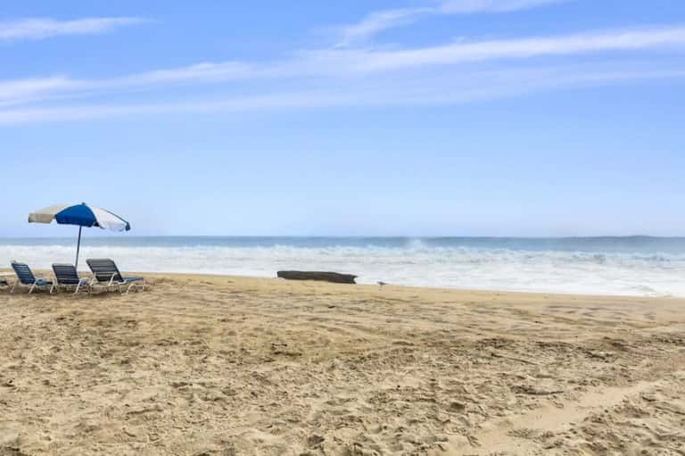 Beach setup with blue and tan umbrella shading lounge chairs facing the ocean