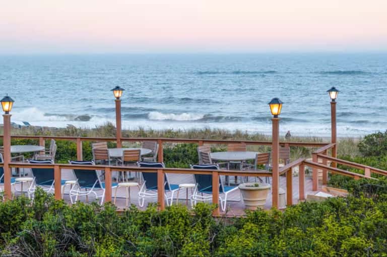 Elevated wooden deck with lounge chairs overlooking beach and ocean at dusk