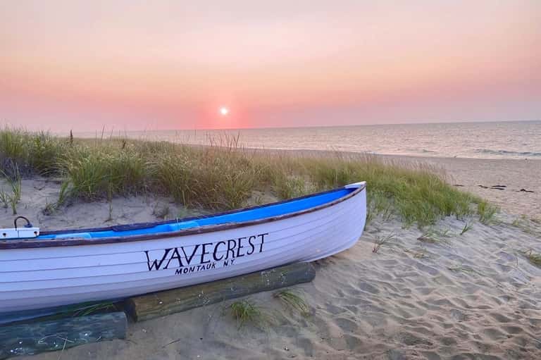 Fishing boat named Wavecrest on beach at sunrise with dune grass and pink sky