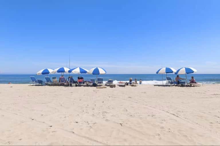 Beach scene with multiple blue and white umbrellas, lounge chairs, and beachgoers