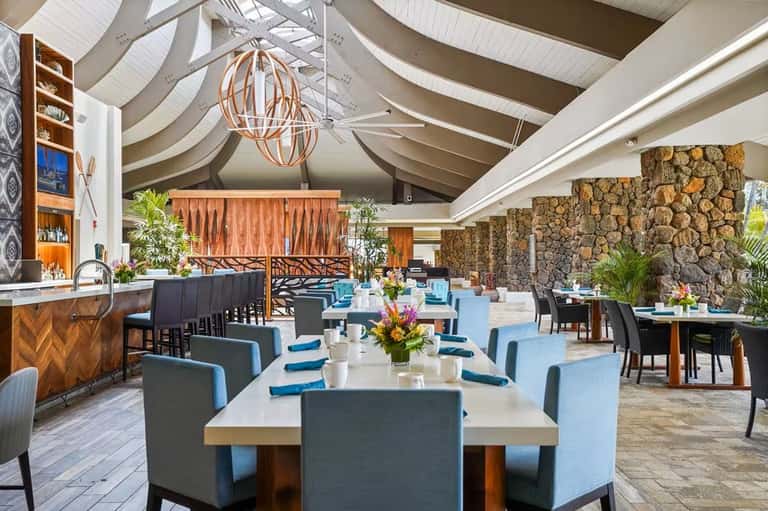 Elegant dining hall with curved white ceiling, hanging globe lights, stone fireplace, and blue-upholstered seating