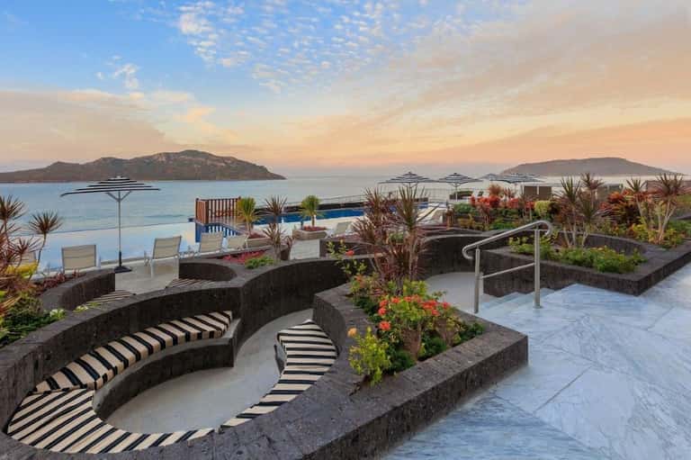 Luxury terrace with curved seating, tropical plants, and infinity pool overlooking islands at sunset