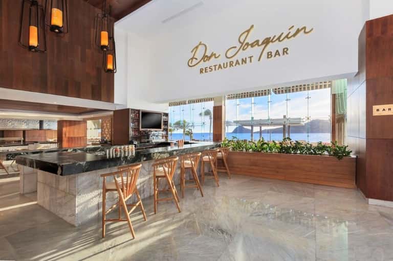 Modern restaurant interior with wood accents, black marble bar, pendant lighting, and panoramic sea views through floor-to-ceiling windows