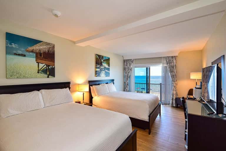 Modern hotel room with two queen beds, ocean view balcony, and tropical wall art décor