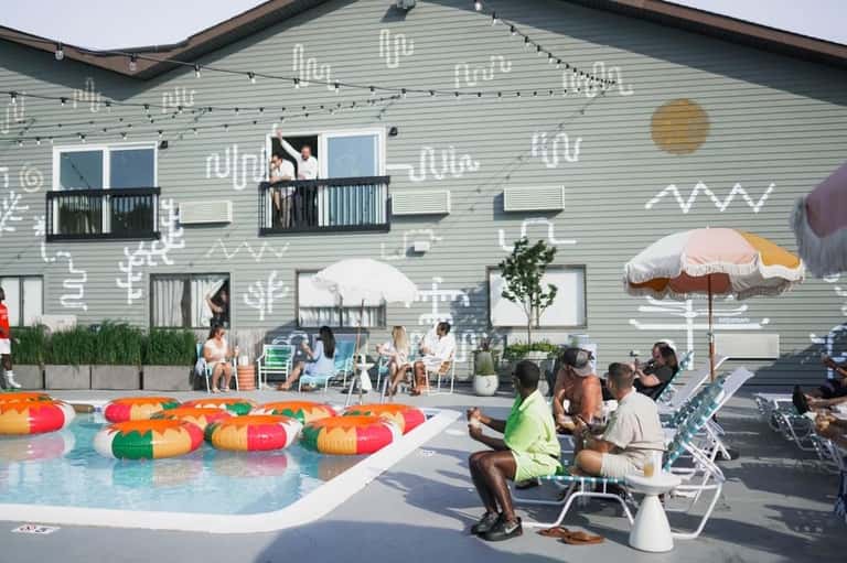 Modern resort pool area with colorful floats, guests lounging in chairs, and building with contemporary mural art