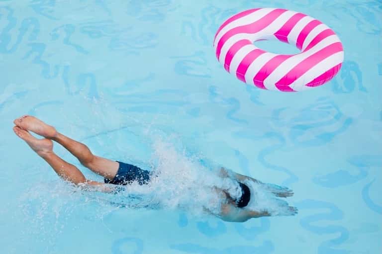 Swimmer doing freestyle stroke in pool with pink and white striped inflatable float nearby